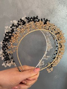 a hand holding a tiara with black and gold beads on it's head