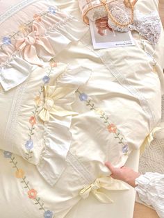 a person is laying on a bed with white sheets and lace trimmings, which are decorated with flowers