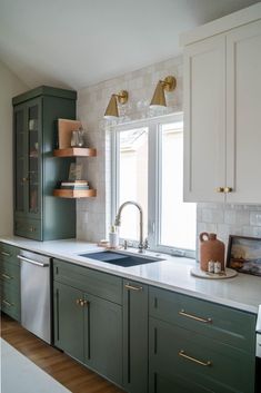 a kitchen with green cabinets, white counter tops and gold pulls on the cupboards