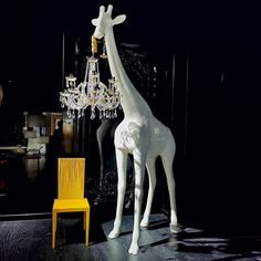 a white giraffe standing next to a yellow chair in a room with chandeliers