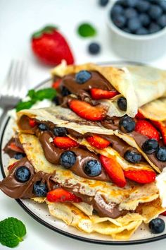 two crepes with chocolate, strawberries and blueberries are on a plate