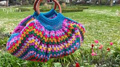 a crocheted bag hanging from a wooden handle in the grass with flowers around it