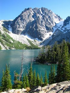 the mountains are covered in snow and green pine trees near a lake with blue water