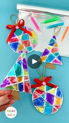 stained glass christmas tree ornament being held by a woman's hand with colored crayons in the background