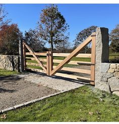 a wooden gate in front of a stone wall and grass area with trees on the other side