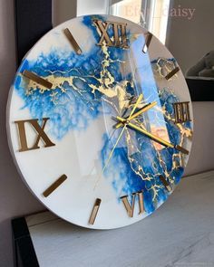 a clock with gold and blue paint on it sitting on a table next to a window