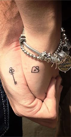 two people holding hands with tattoos on their wrists and wristbands, one has an anchor and the other has a key