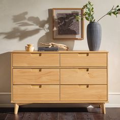 a wooden dresser with two vases on top and one plant in the corner next to it