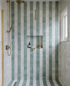 a bathroom with blue and white striped tile on the walls, shower head, and window