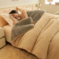 a woman laying on top of a bed covered in a blanket and pillows with her head resting on the pillow