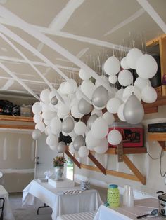 balloons are hanging from the ceiling in a room with white tables and chairs on it