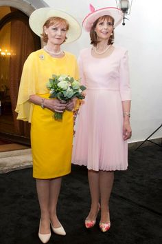 two women standing next to each other in front of a white wall and black carpet