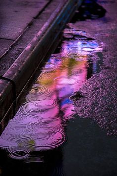 the reflection of a person walking in a puddle with an umbrella on it's side