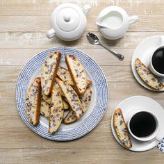 two plates with pastries on them next to cups of coffee and spoons,