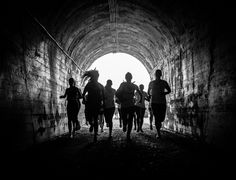 black and white photograph of people running in a tunnel with light coming from the end