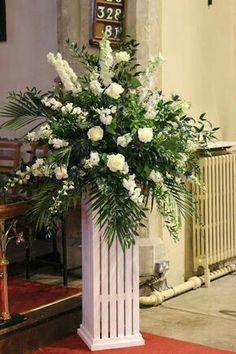 white flowers and greenery are in a tall vase on the floor next to a red rug