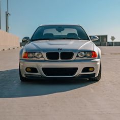 the front end of a silver car parked on top of a parking lot next to a building