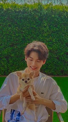 a young man holding a small dog in his lap while sitting on a lawn chair