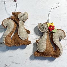 two felt squirrel ornaments hanging from strings on a white wooden surface, one with a flower in it's hair