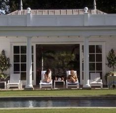 two women lounging on lawn chairs in front of a white house with large windows