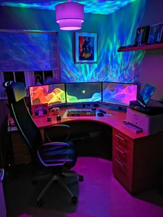 a computer desk topped with two monitors and a keyboard in front of a colorful wall