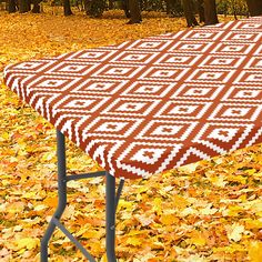 an orange and white table cloth sitting on top of a metal stand in the leaves