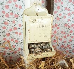 an old fashioned mailbox sitting on top of some dry grass in front of a floral wallpaper