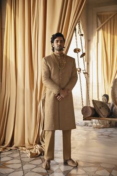 a man standing in front of a curtain wearing a brown suit and gold necklaces