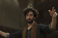 a man with curly hair and beard holding his hands up in the air while wearing a scarf