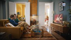 two people sitting on a couch in a living room looking at the television and reading