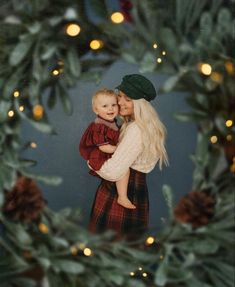 a woman holding a baby in front of a christmas wreath with lights on the background