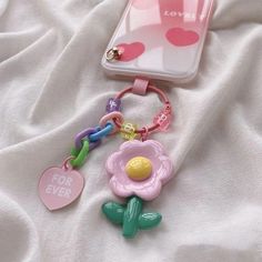 a cell phone and keychain laying on top of a white sheet with a pink flower