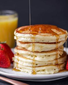 a stack of pancakes with syrup and strawberries on a plate next to a glass of orange juice