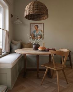 a wooden table sitting under a window next to a painting on the wall in a living room