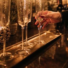 a person is holding a wine glass in front of some champagne glasses on a bar