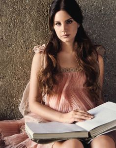 a woman sitting on the ground with an open book in her lap and looking at the camera