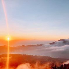 the sun is setting over some mountains with clouds in the foreground and trees on the far side