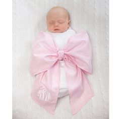 a baby wrapped in a pink bow laying on top of a white blanket with its eyes closed