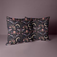 two decorative pillows sitting next to each other on top of a purple surface with pink flowers