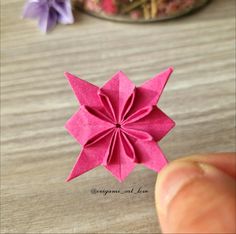 a hand is holding a pink origami flower on a table next to other flowers