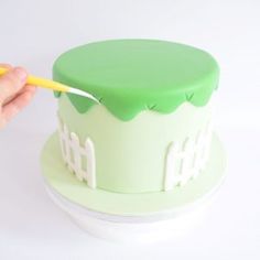 a hand holding a yellow plastic fork over a green and white cake