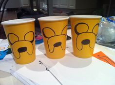 three yellow cups with faces drawn on them sitting on a table next to other items