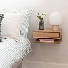 a nightstand with flowers on top of it next to a white wall and a bed