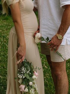 a man and woman standing next to each other with flowers in their hands on the grass