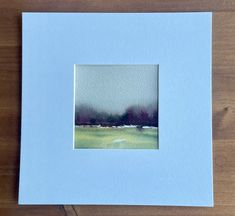 a watercolor painting of a green field with trees in the distance on a wooden table