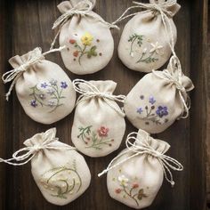 six embroidered bags with flowers on them sitting in front of a wooden box, tied together