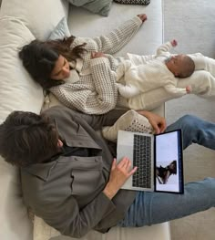 two people sitting on a couch with a laptop and baby in their lap, looking at the screen