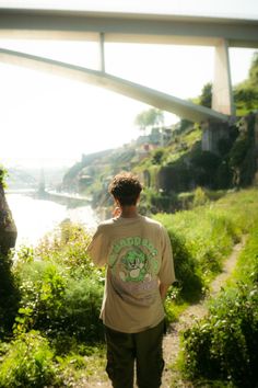 a young man walking down a path next to a river under a bridge overpass