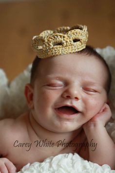 a baby with a golden crown laying on top of it's head and smiling