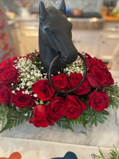 a vase filled with red roses and a black horse head on top of the flowers